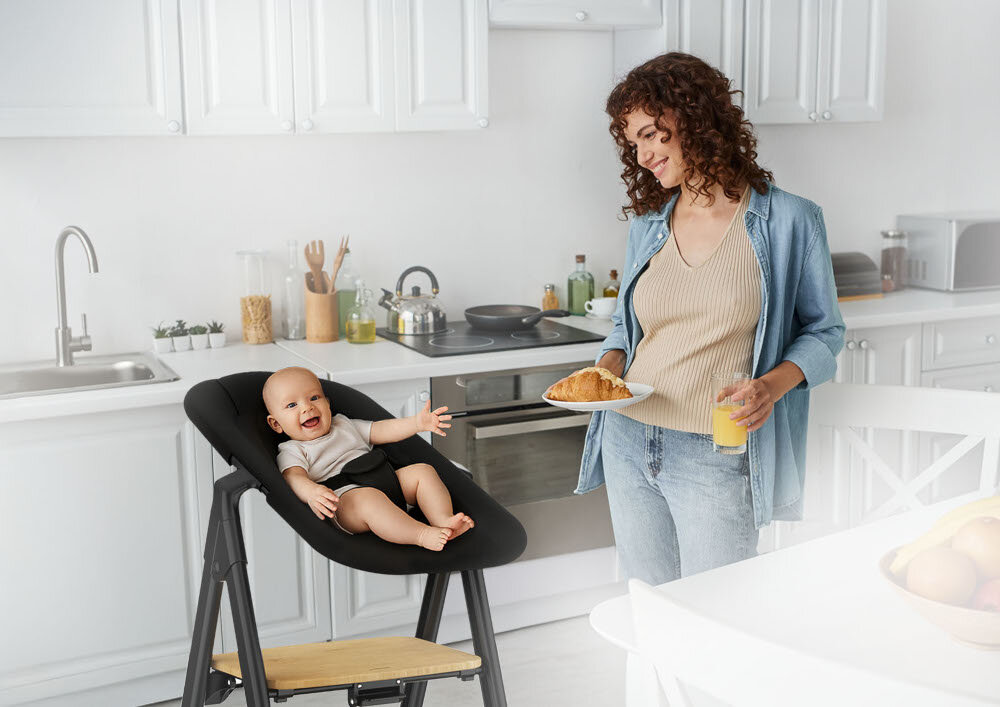 Krzesełko do karmienia NENO Sapori 4w1 Czarny Bezpieczna konstrukcja 3-punktowe pasy stabilna budowa Zaokrąglone krawędzie dziecko leży w leżaczku osoba stoi obok i się uśmiecha