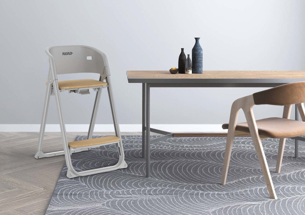 Na obrazie znajduje się szare krzesełko do karmienia z napisem \'neno\' obok drewnianego stołu z trzema butelkami na blacie. W tle widoczny jest wzorzysty dywan i drewniane krzesło.