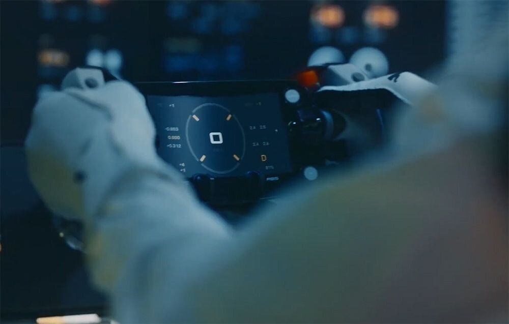 Kierownica MOZA RACING Porsche MISSION R Kierownica z wyświetlaczem trzymana w dłoniach przez kierowcę samochodu sportowego w białym kombinezonie zakrzywiony wyświetlacz OLED przekątna rozdzielczość odświeżanie konstrukcja 300R szkło hartowane ochrona ekranu