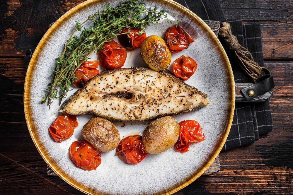 Plan dietetyczny BEDIET 1 miesiąc Pieczony dzwon ryby podany z całymi pieczonymi ziemniakami, pomidorkami koktajlowymi i gałązkami świeżego tymianku na ozdobnym talerzu.