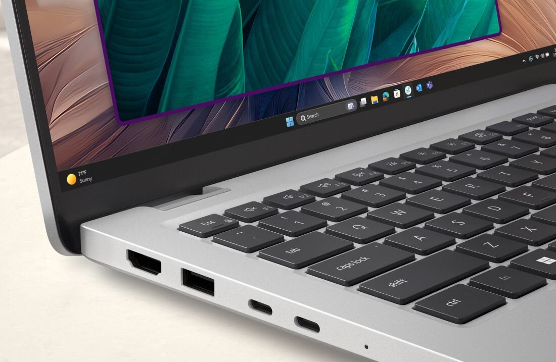 Laptop z widoczną klawiaturą i ekranem, na którym wyświetlany jest pasek z ikonami aplikacji. Obudowa jest srebrna, a na ekranie widoczny jest tekst '77°F Sunny'.