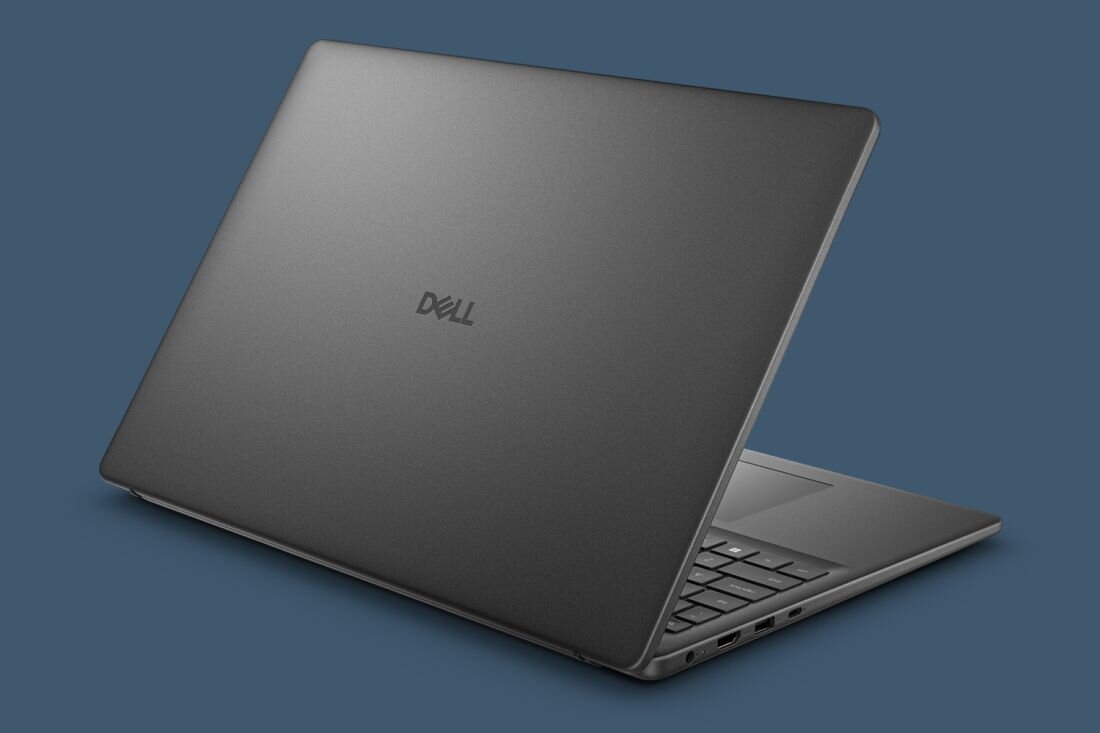 Laptop w kolorze ciemnoszarym z widocznym logo \'Dell\' na pokrywie. Urządzenie jest otwarte, ukazując klawiaturę i porty po boku.