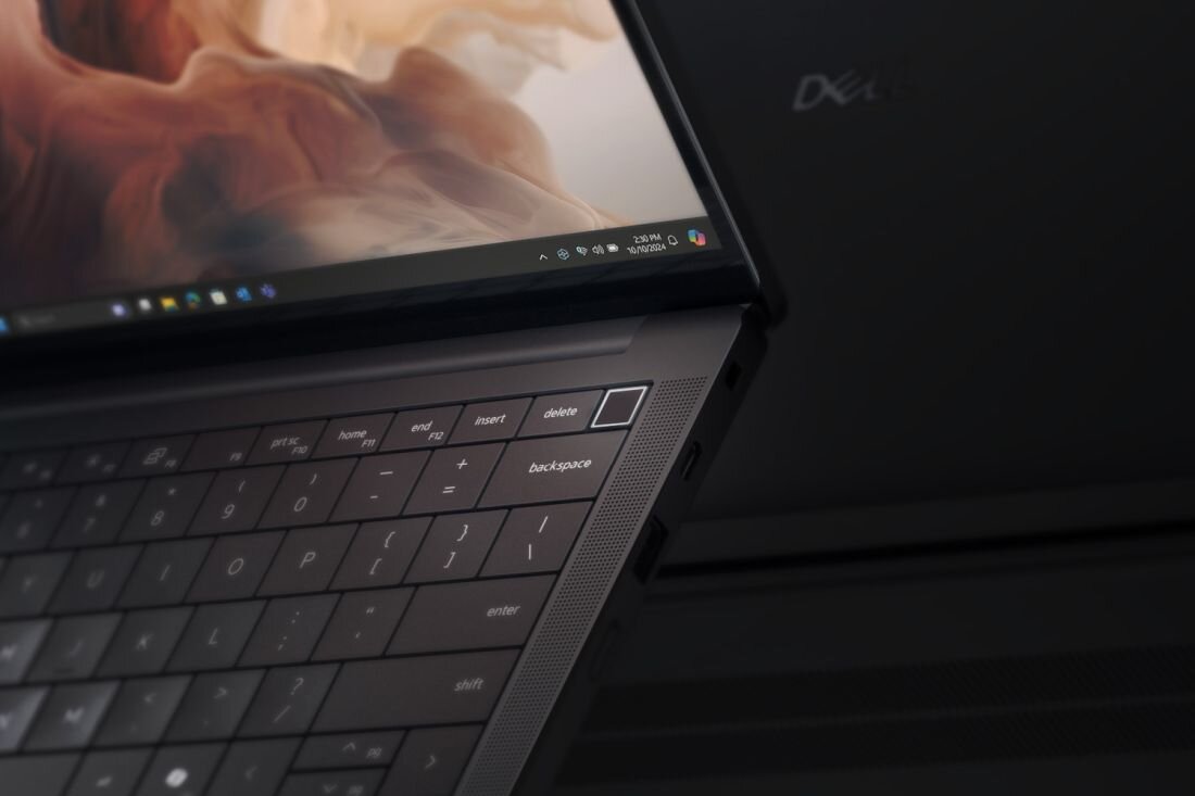 Na zdjęciu widoczny jest laptop z klawiaturą i ekranem, na którym wyświetlany jest abstrakcyjny obraz oraz pasek zadań systemu Windows. Na obudowie laptopa znajduje się logo \'Dell\'.