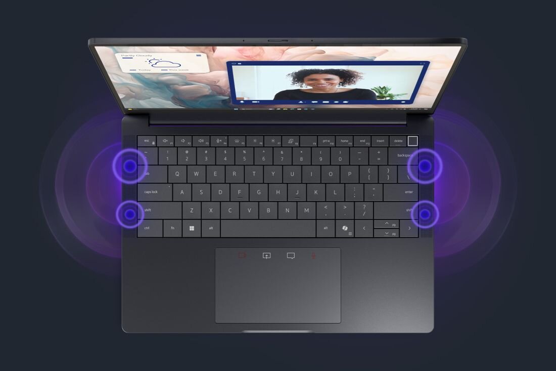 Laptop z otwartym ekranem, na którym widać osobę podczas wideorozmowy. Klawiatura jest podświetlona, a wokół niej widoczne są efekty dźwiękowe w postaci fioletowych okręgów.