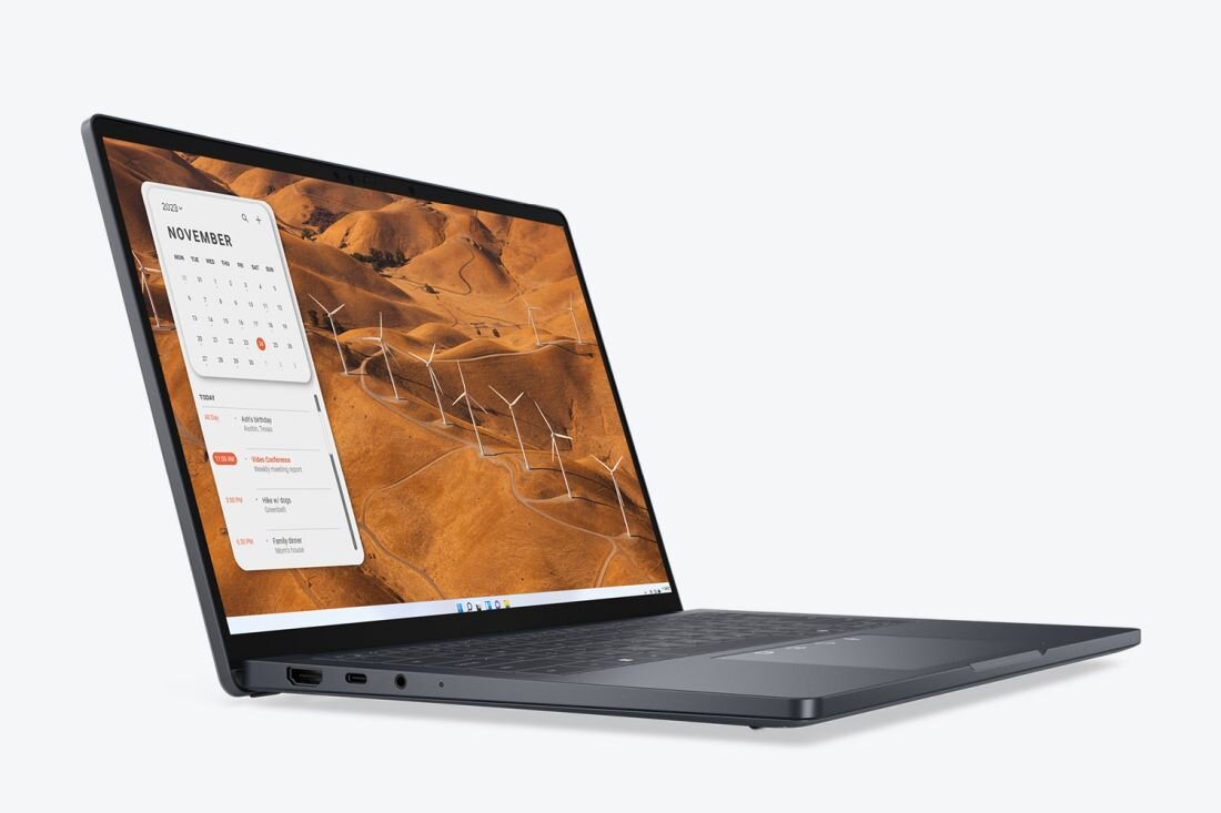 Laptop z otwartym ekranem wyświetlającym kalendarz na listopad oraz krajobraz z wiatrakami. Obudowa jest ciemna, a na boku widoczne są porty.
