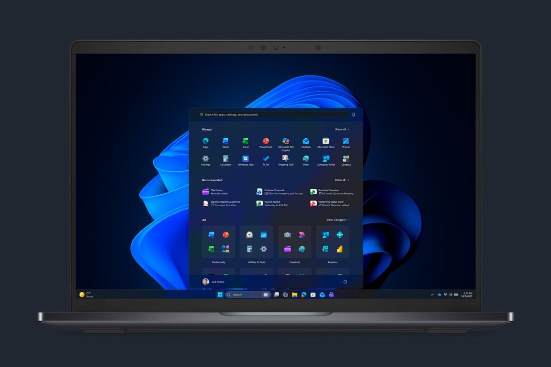 Na obrazie widoczny jest laptop z otwartym ekranem, na którym wyświetlony jest interfejs systemu Windows 11 z menu Start. Tło pulpitu przedstawia niebieską grafikę przypominającą falę.