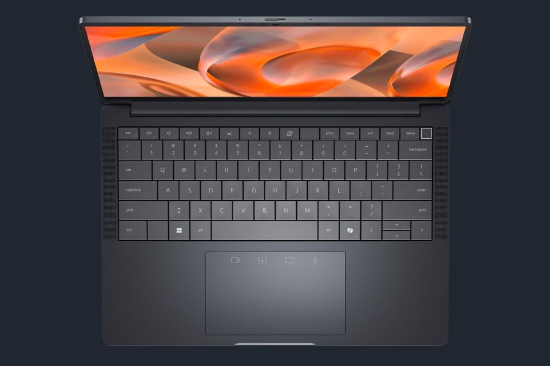 Laptop z otwartym ekranem wyświetlającym abstrakcyjną grafikę w odcieniach pomarańczowego. Klawiatura jest pełnowymiarowa z widocznym touchpadem poniżej.