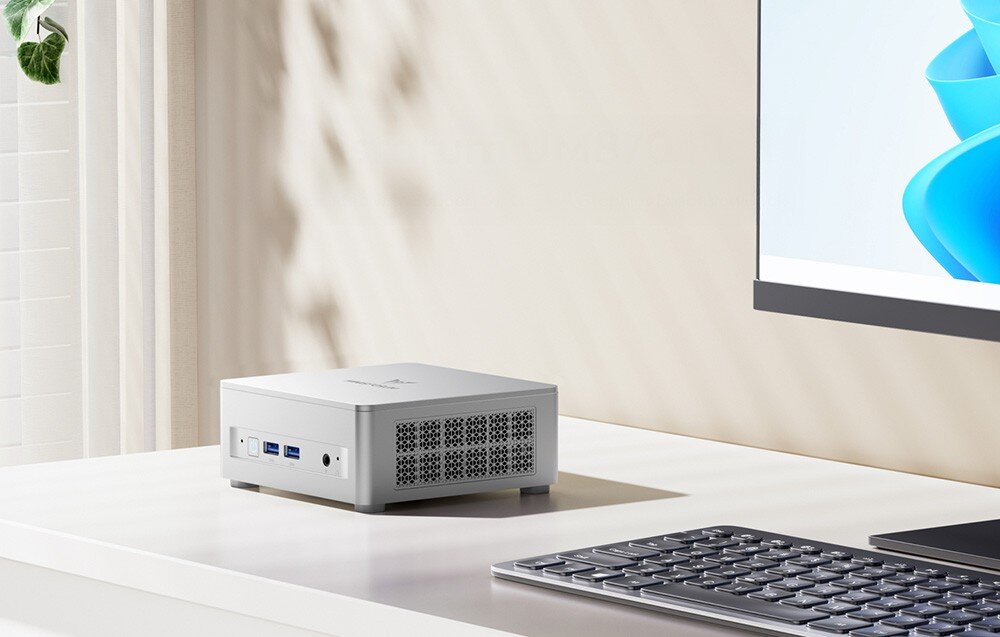 Komputer MINISFORUM UM870 Plus Minimalistyczne stanowisko pracy z mini PC, białą klawiaturą i fragmentem monitora w jasnym pokoju.