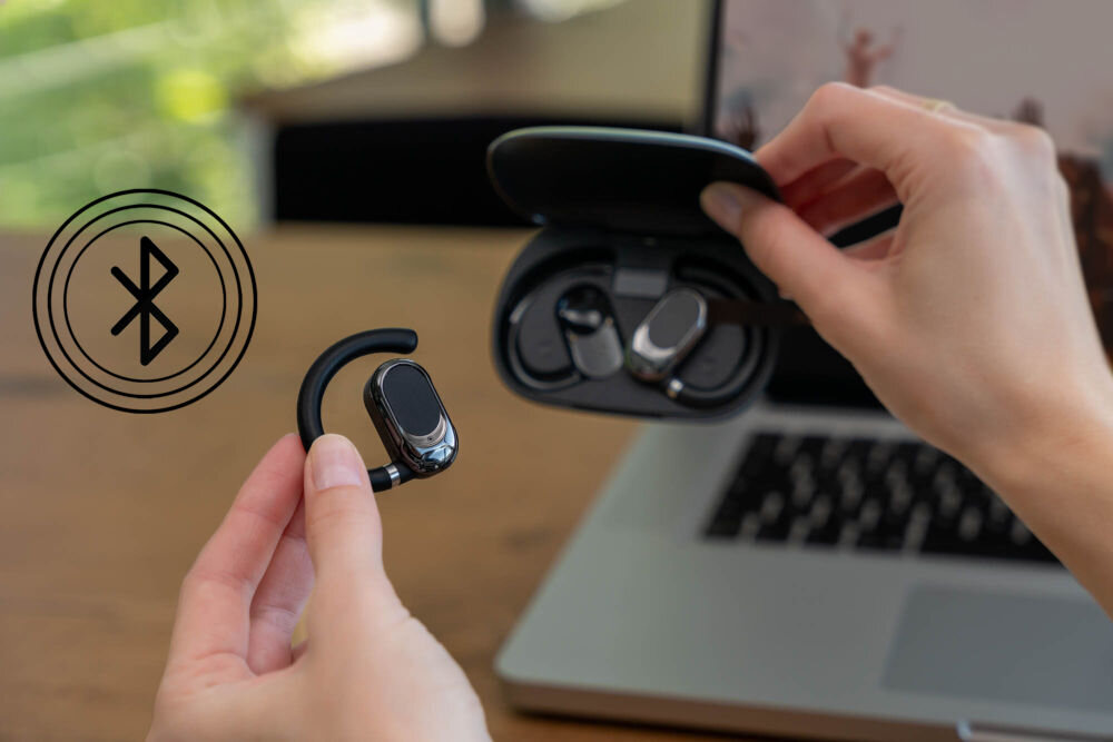 Słuchawki powietrzne XMUSIC XWS550K Czarny Bluetooth 5.3, mikrofon do rozmów, połączenie ze smartfonem i laptopem - osoba trzymajaca w jednej ręce słuchawkę w drugiej etui obok znaczek bluetooth