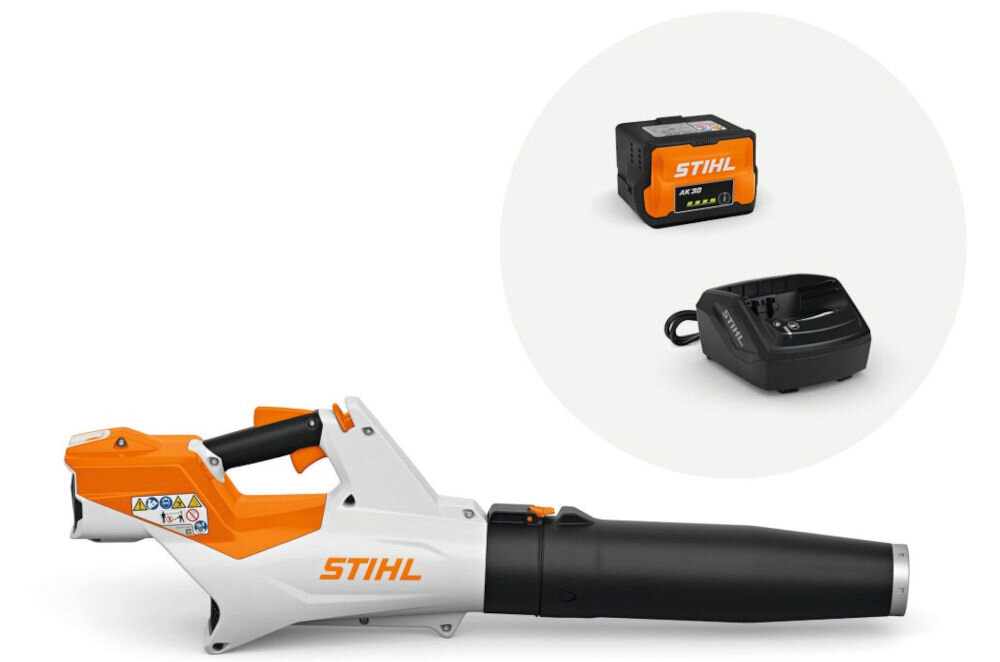 Na obrazie widoczna jest dmuchawa do liści w kolorze białym i pomarańczowym z napisem \'STIHL\'. Obok znajduje się akumulator i ładowarka, również z logo \'STIHL\'.