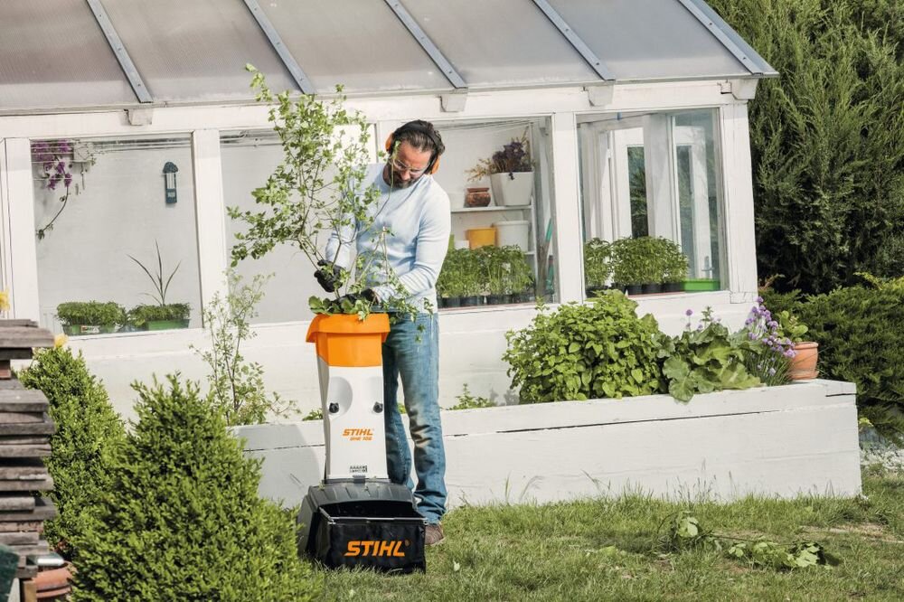 Rozdrabniacz do gałęzi STIHL GHE 105 elektryczny 2200W średnica cięcia 35mm, rozdrabniacz, ogród, sprzątanie, gałęzie, Mężczyzna wrzuca gałęzie z liśćmi do rozdrabniacza.