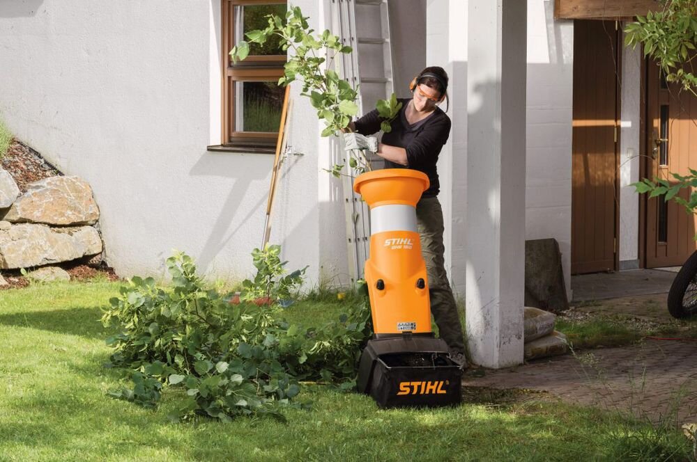 Rozdrabniacz do gałęzi STIHL GHE 150 elektryczny 2500W średnica cięcia 35mm, rębak, rozdrabniacz, gałęzie, ogród, Kobieta wrzucająca ulistnione gałęzie do rozdrabniacza.