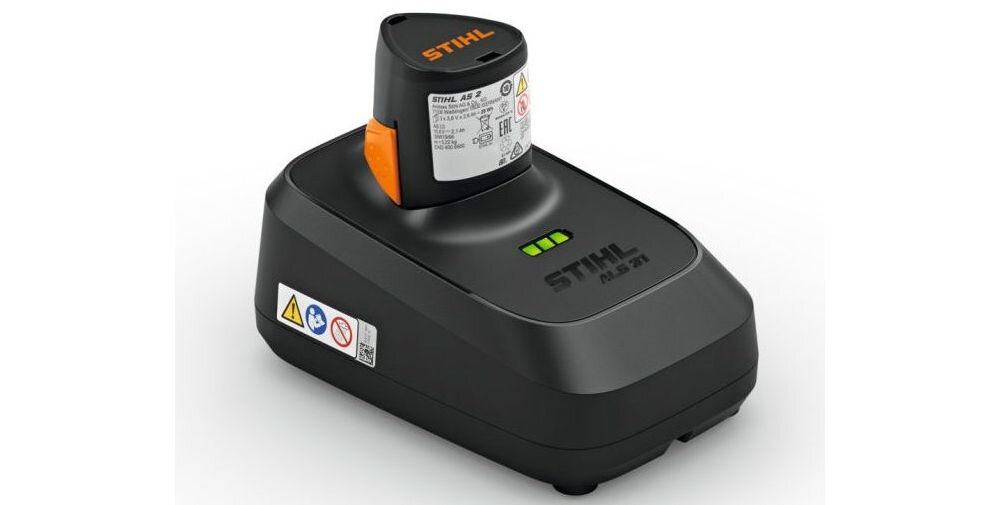 Na obrazie widoczna jest czarna ładowarka z napisem \'STIHL ALS 31\' oraz włożoną baterią z etykietą. Na ładowarce znajdują się trzy zielone diody oraz symbole ostrzegawcze.