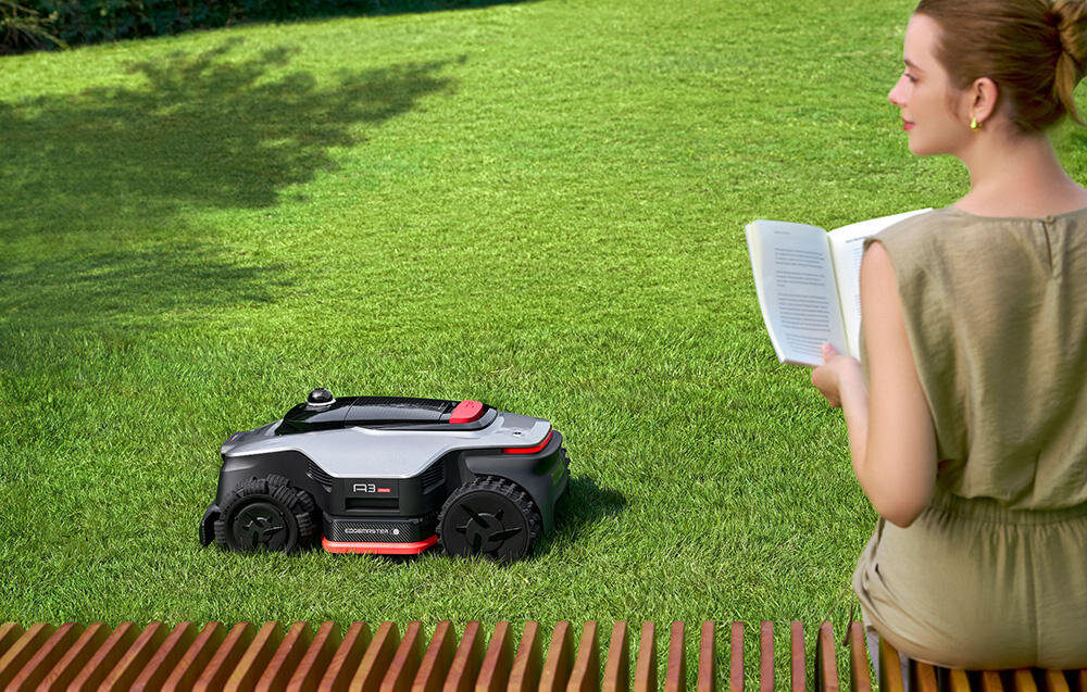 Robot koszący DREAME A3 AWD Pro 3500 trawnik robot kosi trawę na pierwszym planie osoba z książką w dłoni siedzi na ławce specjalny tryb przyjazny zwierzętom funkcja „nie przeszkadzać” robot całkowicie wstrzymuje działanie