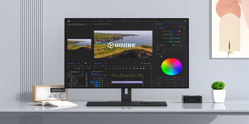 Komputer QOOBE II AP13620 Komputer mini PC obok monitora wyświetlającego program do edycji wideo, na biurku z dekoracjami i klawiaturą, wielkość, wymiary, procesor, rdzenie, przeznaczenie