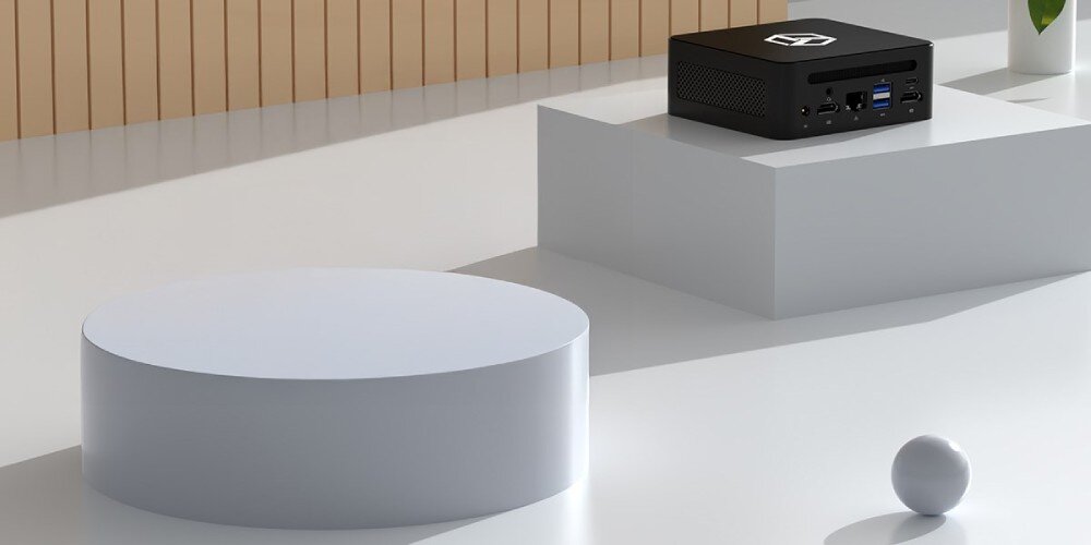 Komputer QOOBE II AP13620 Czarny miniaturowy komputer ustawiony na białym podwyższeniu w jasnym, minimalistycznym otoczeniu, pamięć RAM, taktowanie, rozbudowa