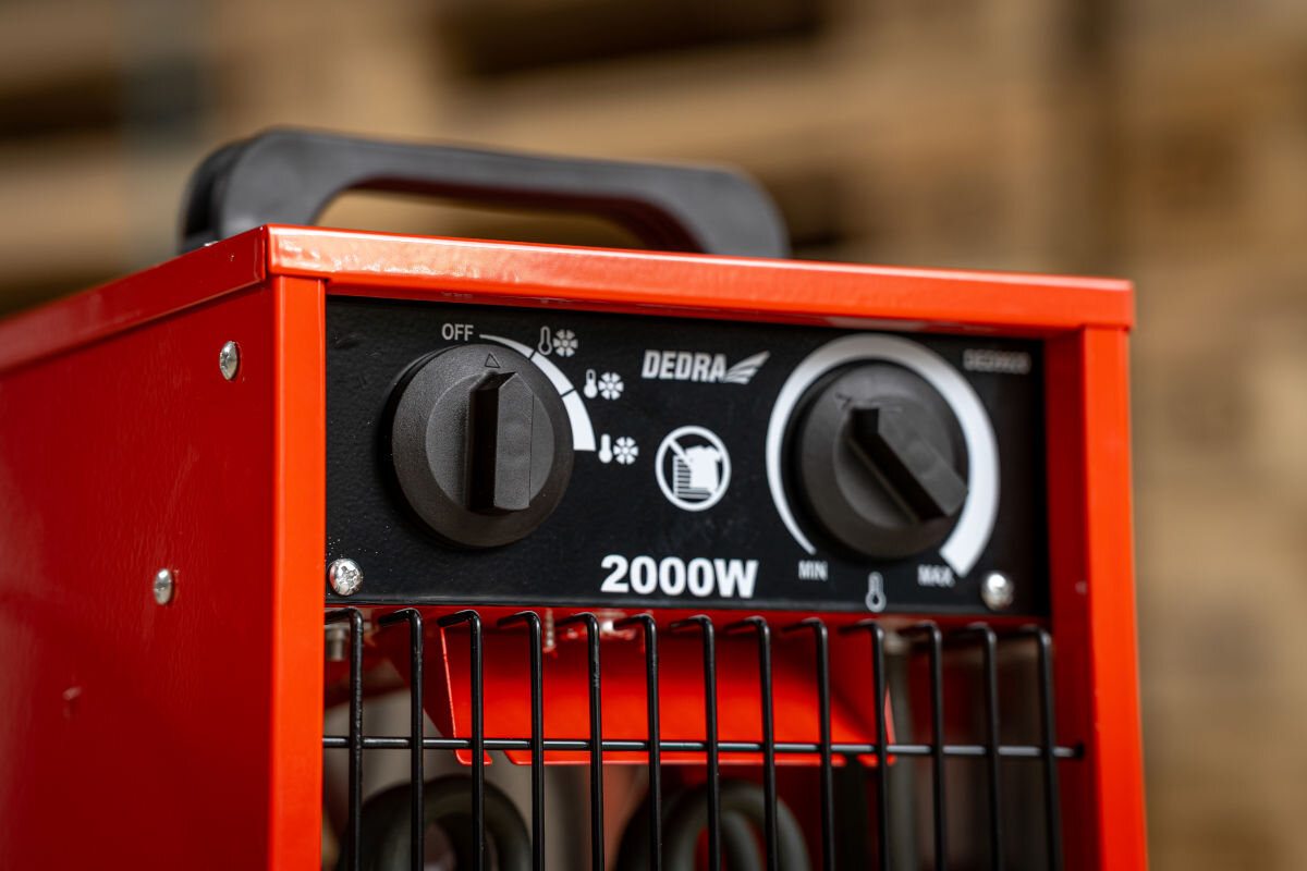 Nagrzewnica elektryczna DEDRA DED9920, chłodny, ciepły, gorący, wentylator, Mężczyzna trzyma nagrzewnicę DEDRA DED9920 w magazynie z paletami, widok frontowy.