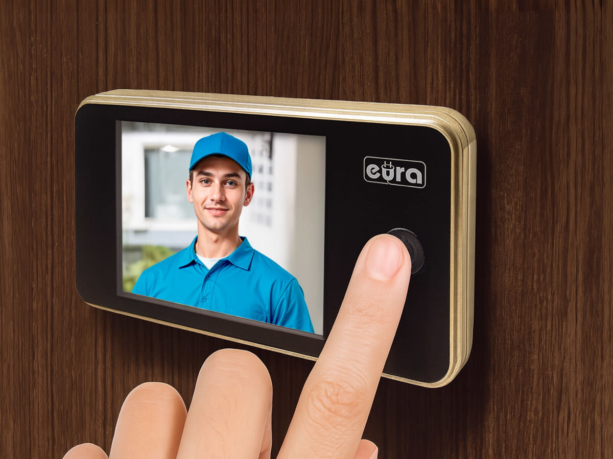 Wideo-wizjer EURA VDP-01C1 Eris Złoty, przycisk, monitor, LCD, komunikacja, na drewninanym tle palec dotyka wideowizjer zamontowany do ściany