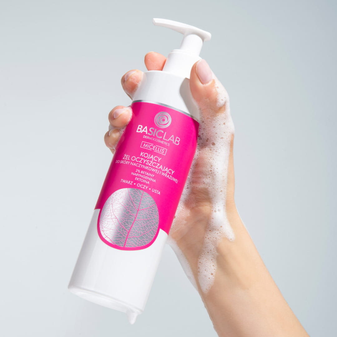 Ręka trzyma butelkę z pompką, na której widnieje etykieta z napisem: \'BASICLAB DERMOCOSMETICS MICELLIS KOJĄCY ŻEL OCZYSZCZAJĄCY DO SKÓRY NACZYNKOWEJ I WRAŻLIWEJ Z 2% PANTHENOLU, NIACYNAMIDU, ECTOINA TWARZ • OCZY • USTA\'.