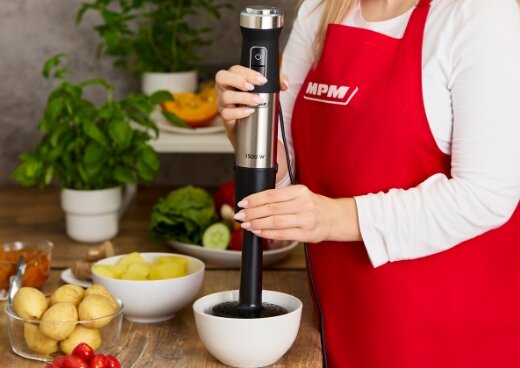 Kobieta miksuje ziemniaki blenderem z przystawką do puree. Obok miski z ziemniakami.