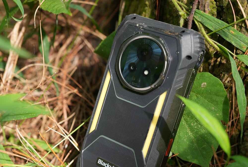 Smartfon z dużym obiektywem aparatu, umieszczony na tle zielonych liści i trawy. Na obudowie widoczny jest napis \'Blackview\'.