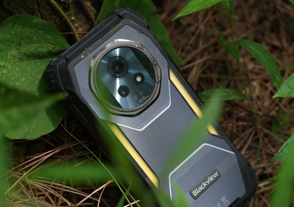 Smartfon z widocznym logo \'Blackview\' leży na ziemi wśród zielonych liści. Urządzenie ma solidną obudowę i widoczny aparat fotograficzny.