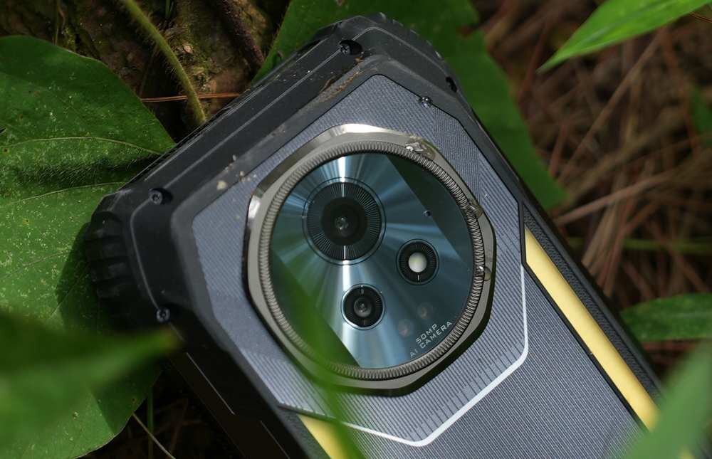 Smartfon z trzema obiektywami aparatu, umieszczony na tle zielonych liści. Na obudowie widoczny jest napis \'50MP AI Camera\'.