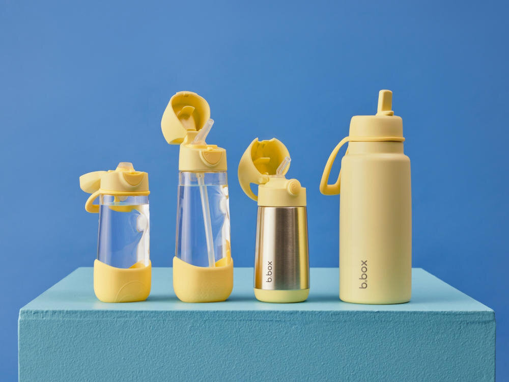 Na niebieskim tle znajdują się cztery żółte butelki o różnych kształtach i rozmiarach, z widocznym logo \'b.box\'.