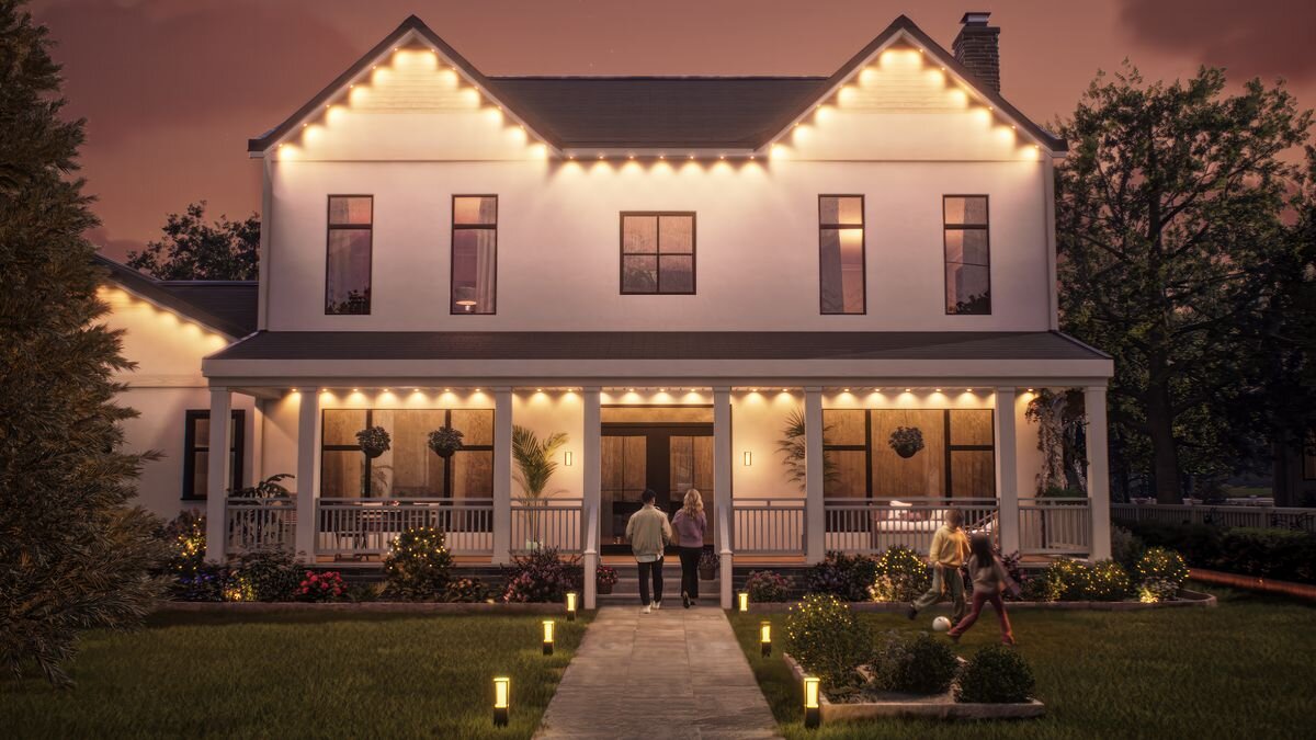 Girlanda ogrodowa PHILIPS HUE Festavia (moduł przedłużający 9 m), kolory, temperatura, 1000K, aplikacja, Dom oświetlony ciepłym, białym światłem i rodzina bawiąca się na zewnątrz.