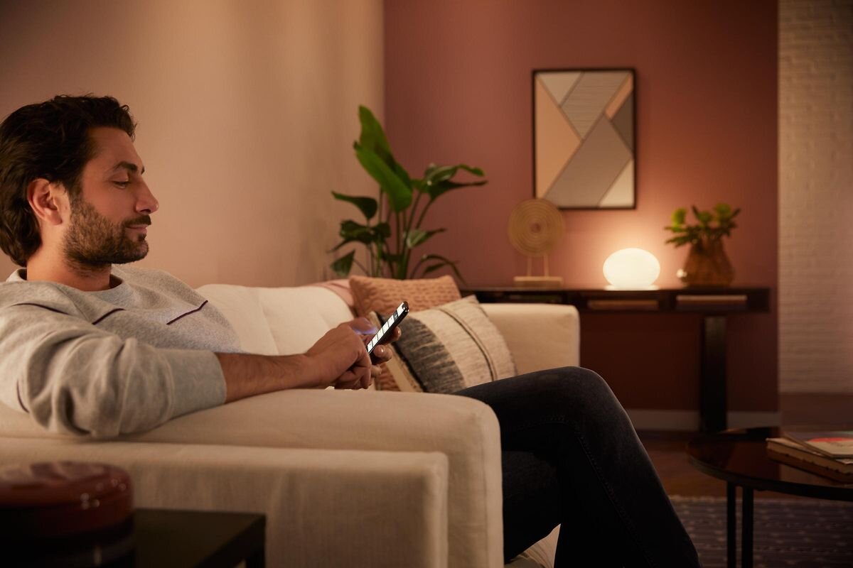 Lampa biurkowa PHILIPS HUE Flourish (Bluetooth, ZigBee), biały, 2000K, 6500K, chłodne, Mężczyzna sterujący oświetleniem Philips Hue za pomocą smartfona.