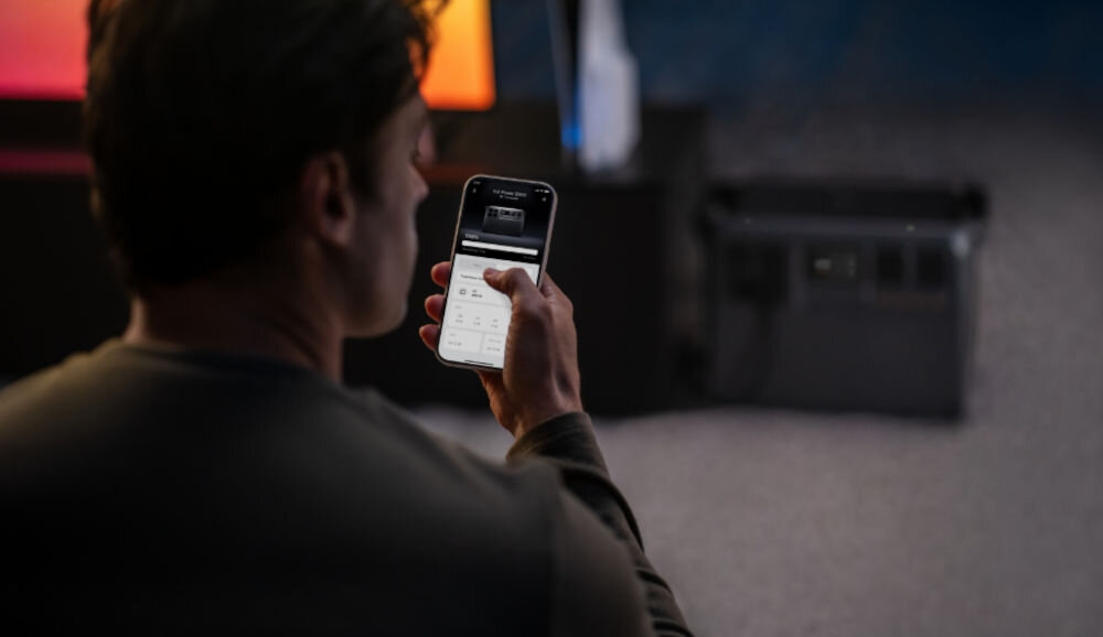 Stacja zasilania DJI Power 2000 2048 Wh Bank energii, zarządzanie, aplikacja, anroid, ios, mężczyzna obsługuje aplikację na telefonie w pokoju