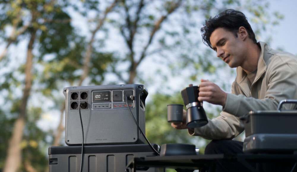 Stacja zasilania DJI Power 2000 2048 Wh Bank energii, gniazdko, energia, ładowanie, fotowoltaiczne, mężczyzna nalewa sobie napoju, obok stacja stoi na skrzyni