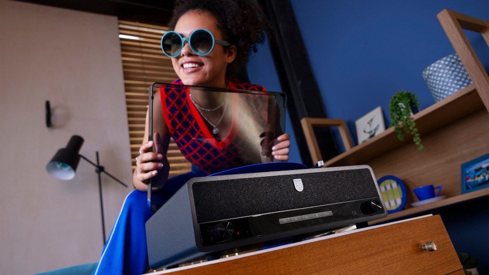 PHILIPS TAV3000B/10 gramofon Bluetooth funkcje bezprzewodowe, osobra trzymająca pokrywę gramofonową w rękach, gramofon stojący na szafce