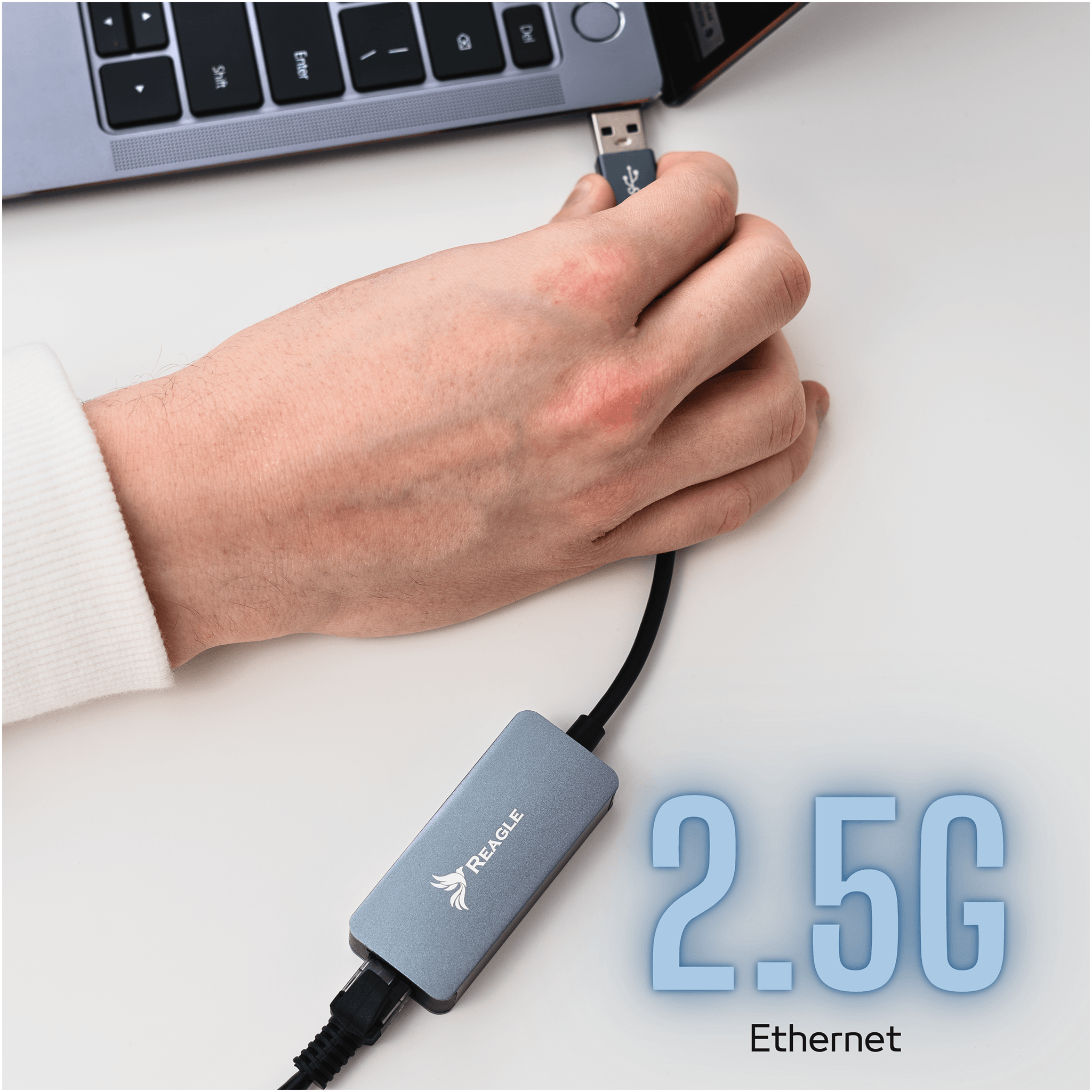 Osoba podłącza srebrny adapter REAGLE do portu USB laptopa. Na adapterze widoczne jest logo REAGLE, a obok napis \'2.5G Ethernet\'.