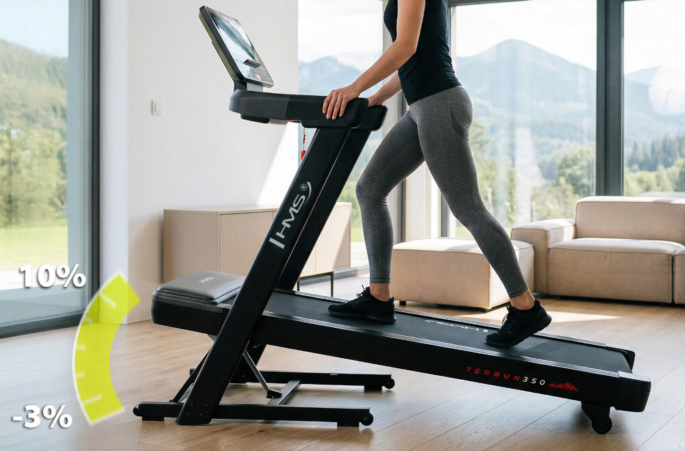 Bieżnia elektryczna HMS TERRUN350 1305W 22 km-h dom pokój osoba korzysta z bieżni w tle duże okno kanapa strzałka pokazująca możliwość regulacji kąta nachylenia dwukierunkowa regulacja nachylenia od -3% do 10% podbiegi i zbiegi płynna zmiana kąta wytrzymałość wspiera regularność ćwiczeń