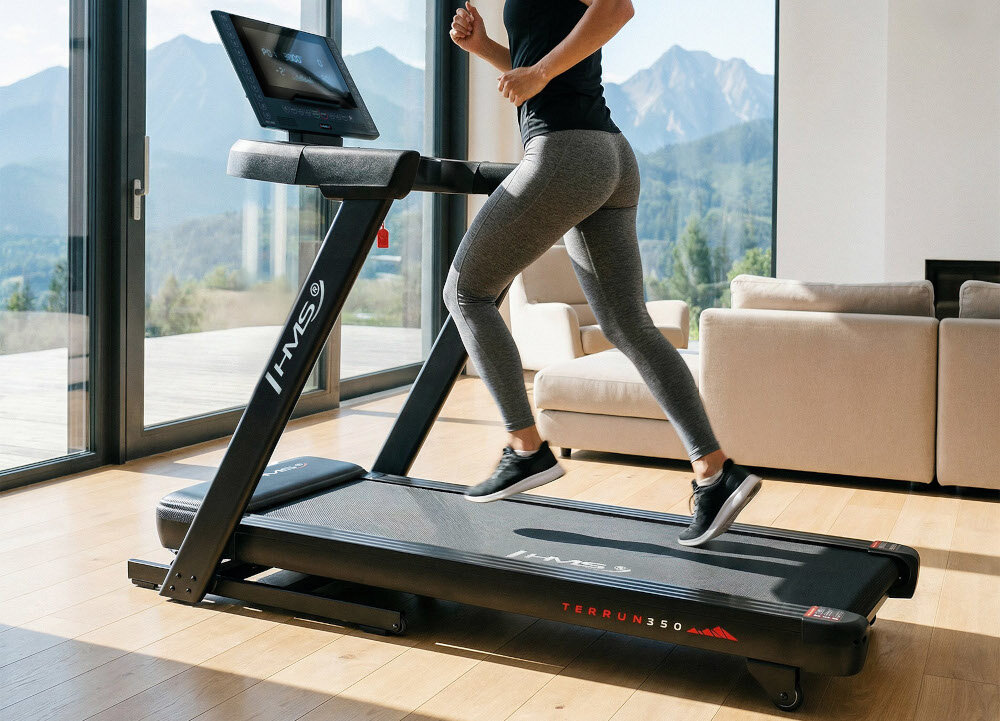 Bieżnia elektryczna HMS TERRUN350 1305W 22 km-h dom pokój osoba korzysta z bieżni w tle duże okno kanapa zakres prędkości 1–22 km/h płynna regulacja komfort i kontrola tempa regularne treningi motywuje do codziennej aktywności