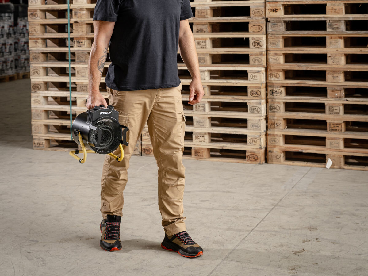 Nagrzewnica elektryczna DEDRA DED9931B, lekkość, uchwyt, stabilność, ergonomia, Mężczyzna niesie nagrzewnicę DEDRA DED9931B za uchwyt w magazynie z paletami, ujęcie całości.