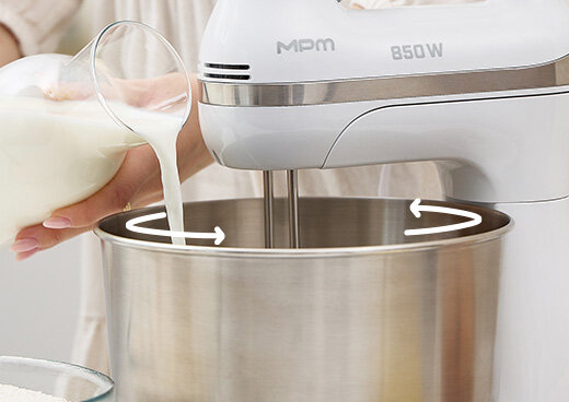 Osoba wlewa mleko do misy  obrotowej miksera MMR-26Z/B. Białe zaokrąglone strzałki symbolizują ruch misy.