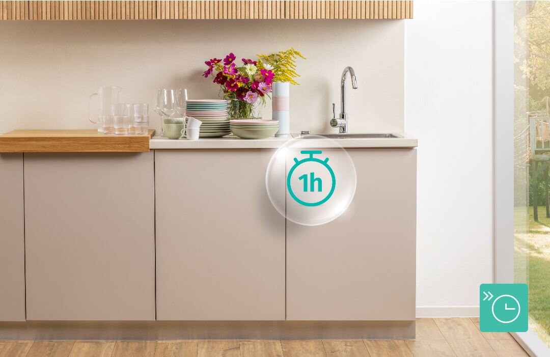 ZMYWARKA GORENJE GV520E15 Jasna kuchnia z naczyniami i bukietem kwiatów ustawionymi na blacie nad zmywarką, na froncie mebli umieszczono ikonę zegara „1h”, sugerując szybki program mycia w jednej godzinie