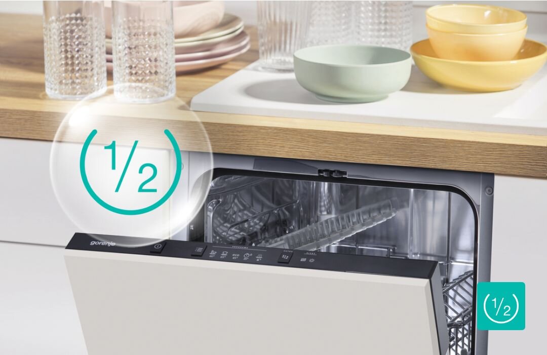 ZMYWARKA GORENJE GV520E15 Otwarta częściowo zmywarka do zabudowy z widocznym wnętrzem i panelem sterowania, nad nią na blacie stoją szklanki i miski, a grafika „1/2” wskazuje możliwość włączenia programu przy połowie załadunku