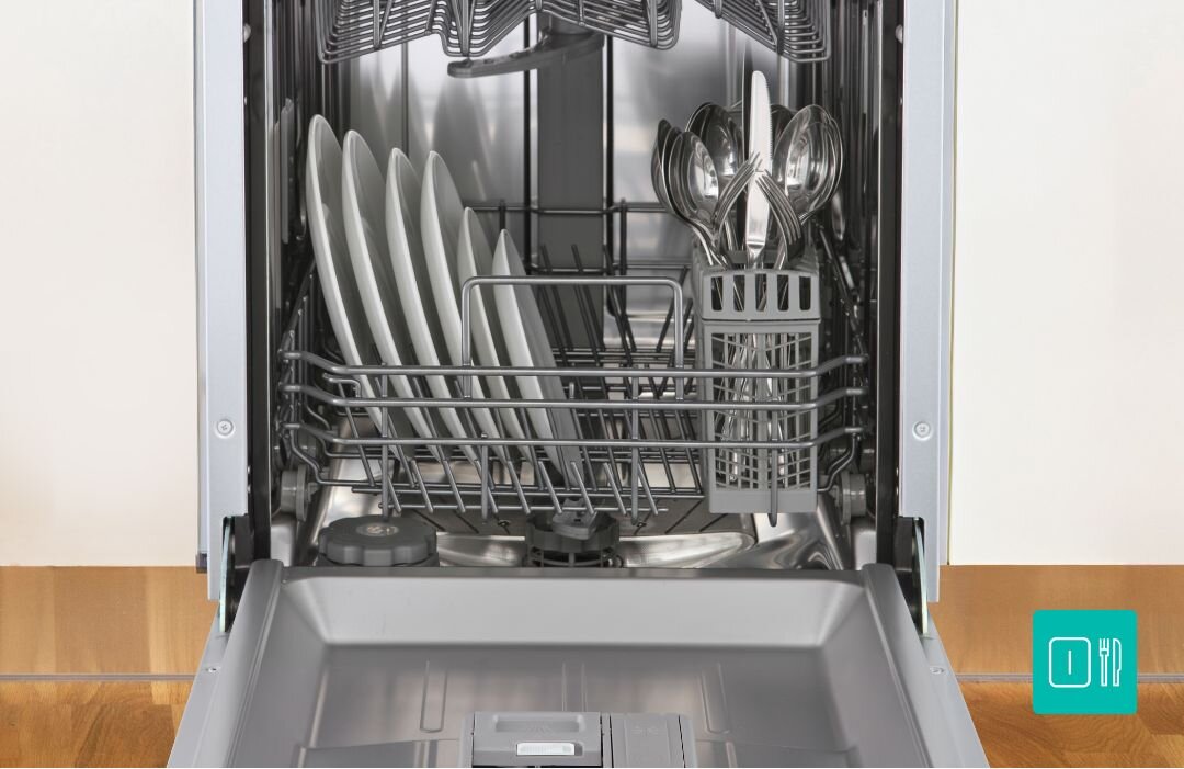 ZMYWARKA GORENJE GV520E15 Otwarta zmywarka z dolnym koszem wypełnionym talerzami oraz koszykiem na sztućce, ustawiona na tle drewnianej podłogi, co podkreśla wygodne rozmieszczenie naczyń