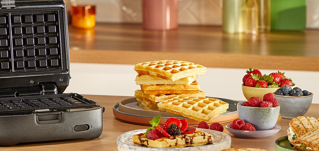 Otwarty opiekacz SW862B na stole. Obok talerz z porcją gofrów i świeże owoce.