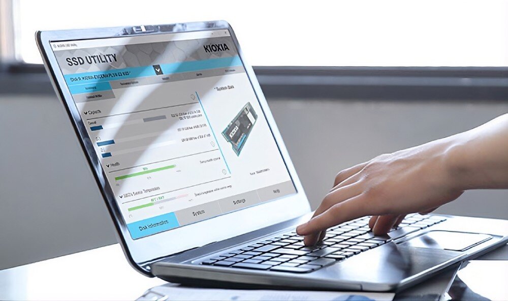 Dysk KIOXIA Exceria Pro G2 Otwarty laptop wyświetlający na ekranie program 'SSD UTILITY' firmy Kioxia z widocznymi paskami postępu i grafiką dysku, obok dłoń na klawiaturze, trwałość, żywotność, oprogramowanie