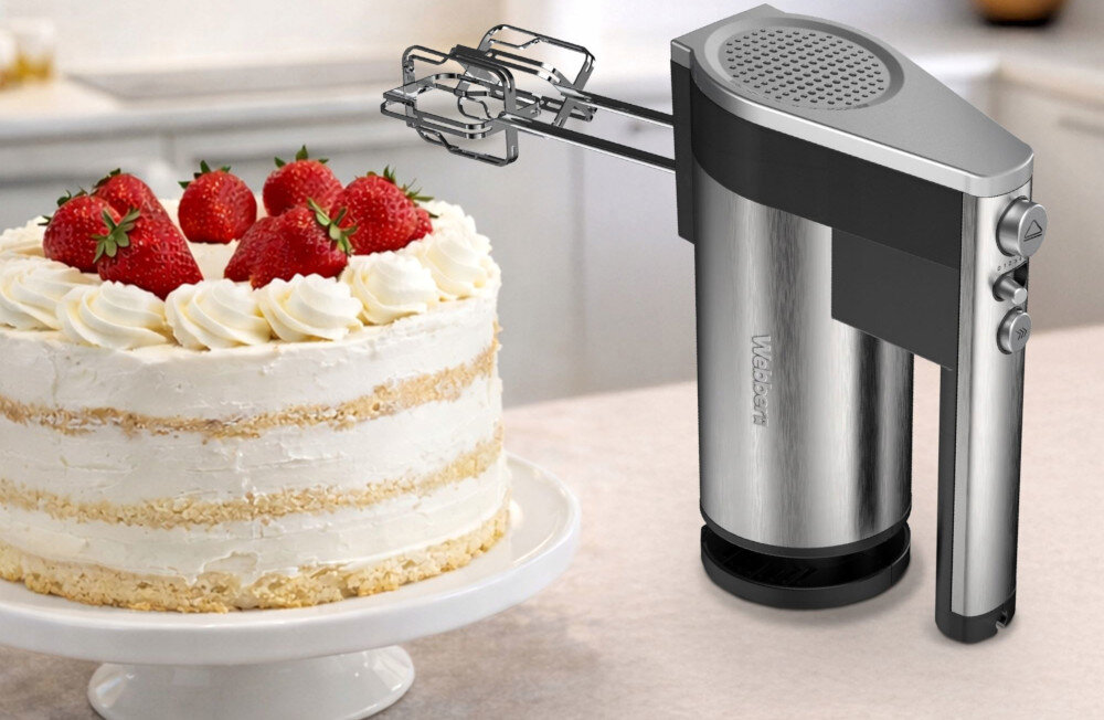 Na blacie kuchennym znajduje się tort udekorowany bitą śmietaną i truskawkami. Obok stoi mikser ręczny z metaliczną obudową i widocznym logo \'WEBBER\'.