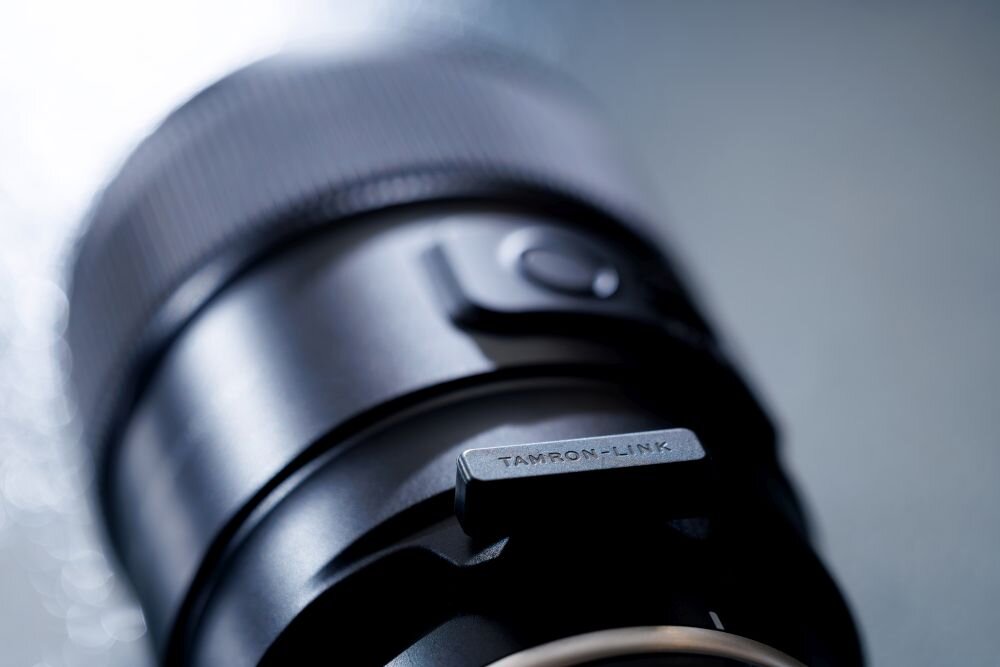 Zbliżenie na czarny obiektyw fotograficzny z widocznym napisem \'TAMRON-LINK\'.