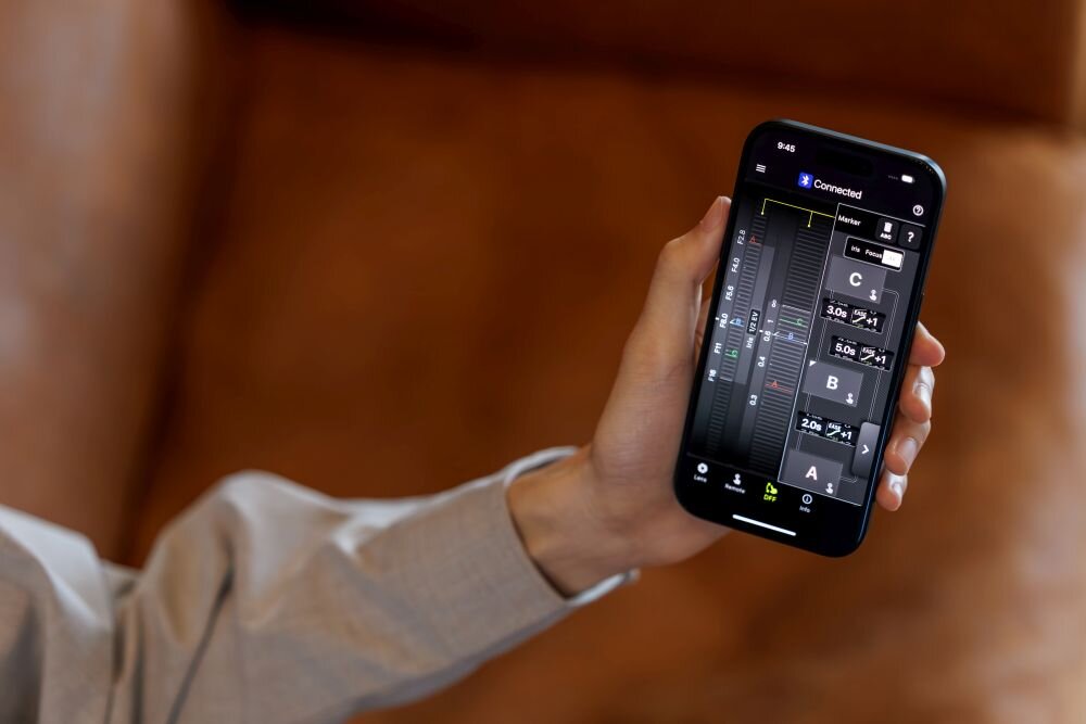 Osoba trzyma smartfon z wyświetlonym interfejsem aplikacji do miksowania dźwięku. Na ekranie widoczne są suwaki i oznaczenia literowe A, B, C oraz tekst \'Connected\'.