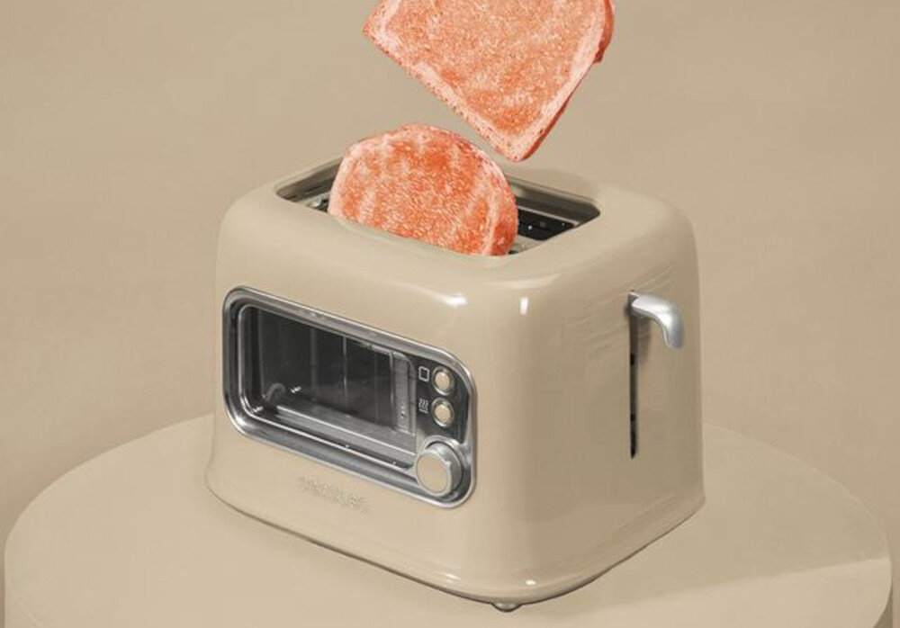 Beżowy toster z dwoma kromkami chleba unoszącymi się nad nim. Na tosterze widoczne są przyciski i pokrętło, a na obudowie napis \'CECOTEC\'.