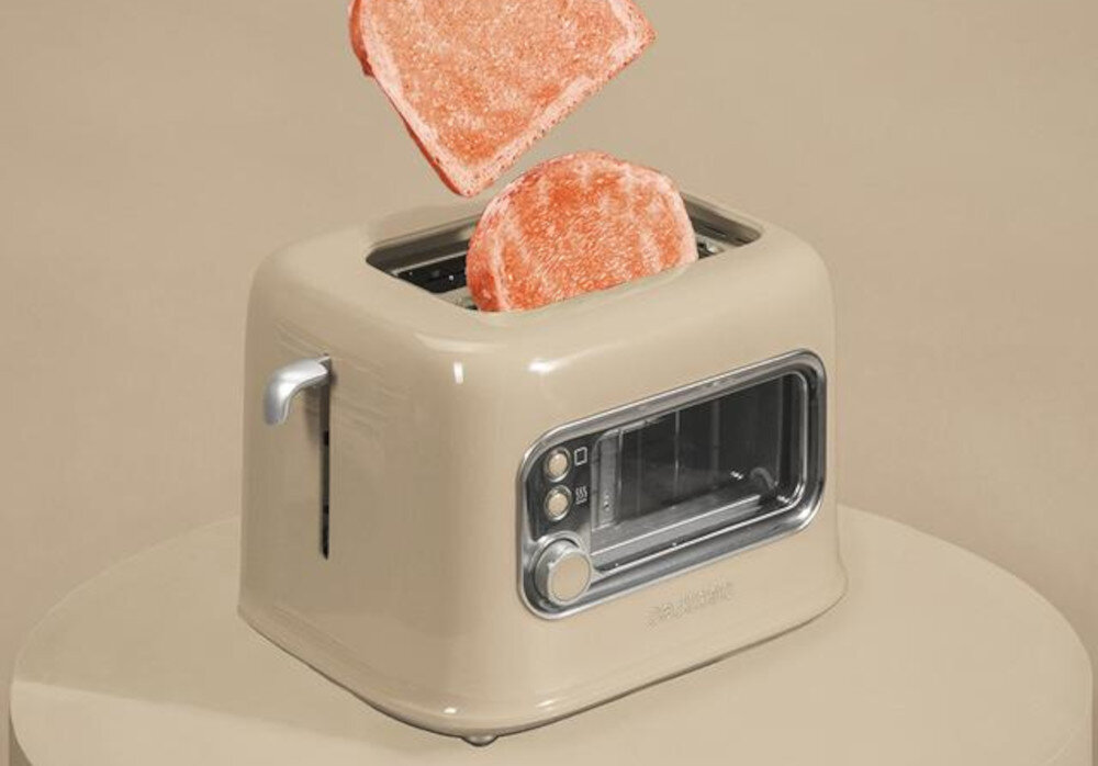 Beżowy toster z przezroczystym panelem i dwoma przyciskami, z którego wyskakują dwa kawałki pieczywa. Na tosterze widoczne jest logo \'CECOTEC\'.