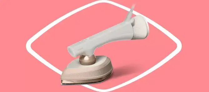 Na różowym tle znajduje się parownica do ubrań w kolorze białym i złotym. Urządzenie ma nowoczesny design i jest ustawione pod kątem, co ukazuje jego profil.