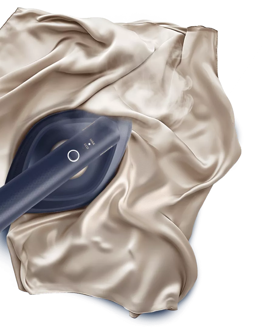 Na obrazie widać parownicę do ubrań przesuwającą się po gładkiej, jasnej tkaninie, z której unosi się para. Na parownicy widoczny jest napis \'MAX ECO\'.